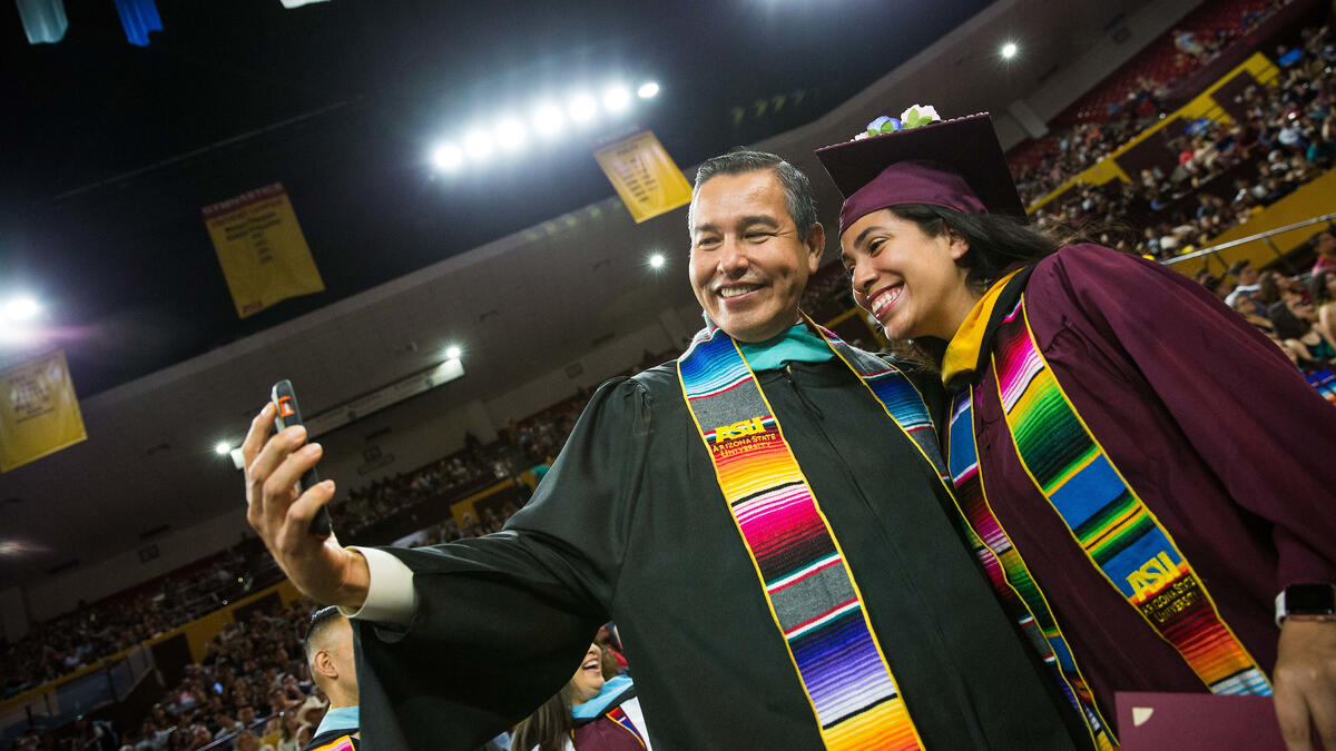 Two Hispanic students in commencement regalia pose for a selfie